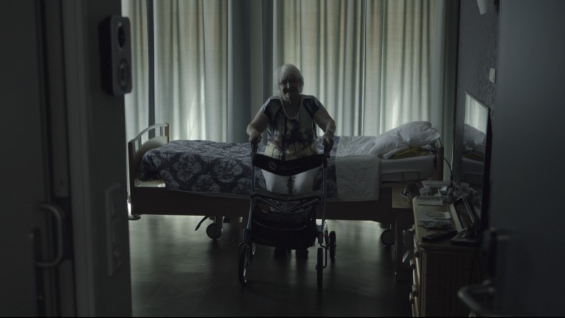 Gabri Christa's mom, Magdalena sitting on the edge of a bed with her walker, a still shot from Christa's film